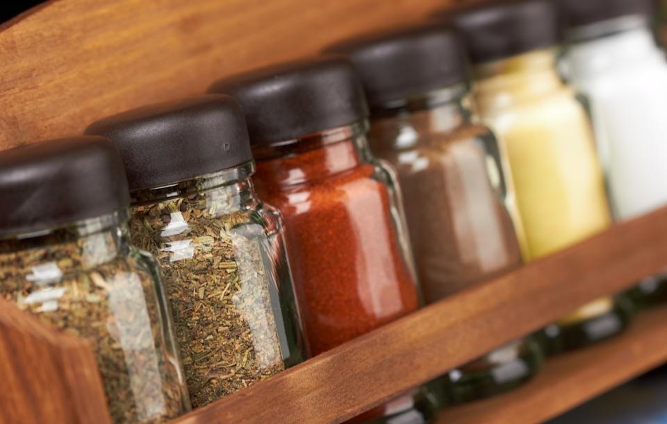 Various spices in glass jars with black lids are neatly arranged on a wooden rack