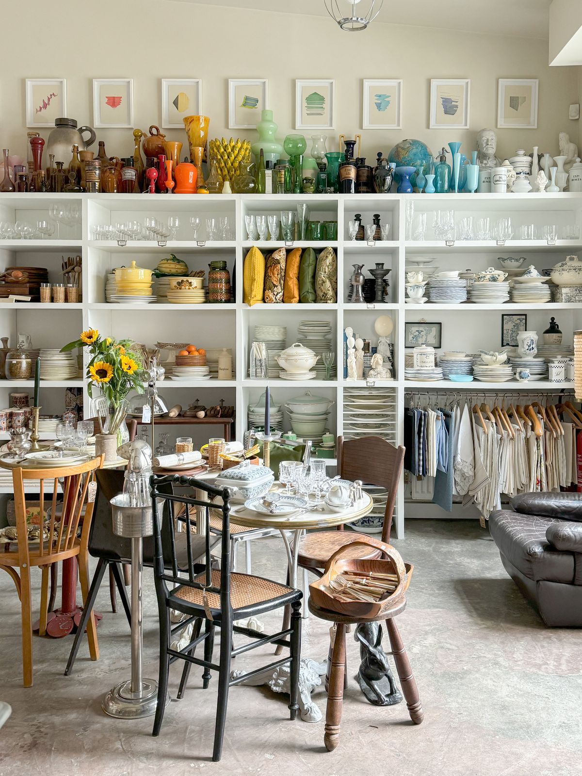 A cafe table set with porcelain in front of shelves holding home goods, including stacks of plates, pillows, and glassware.