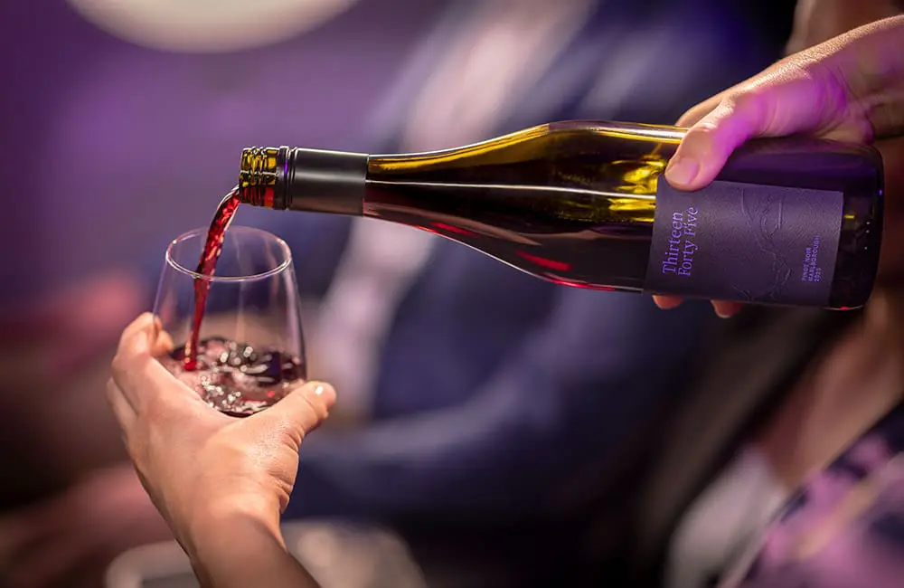 Hand pouring pinot noir from Thirteen Forty Five bottle on Air New Zealand aircraft