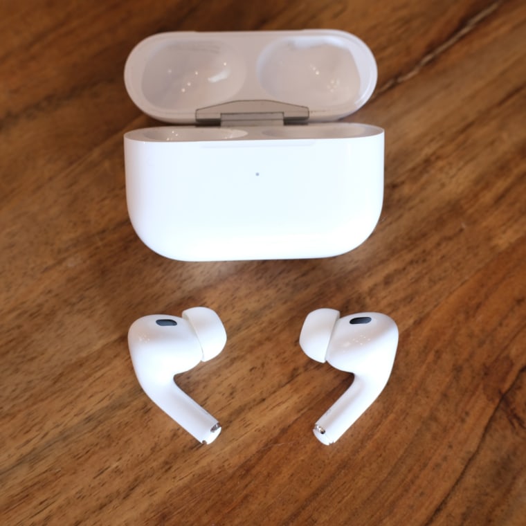 A close up of the Apple AirPods Pro 2 earbuds and charging case against a wood background.
