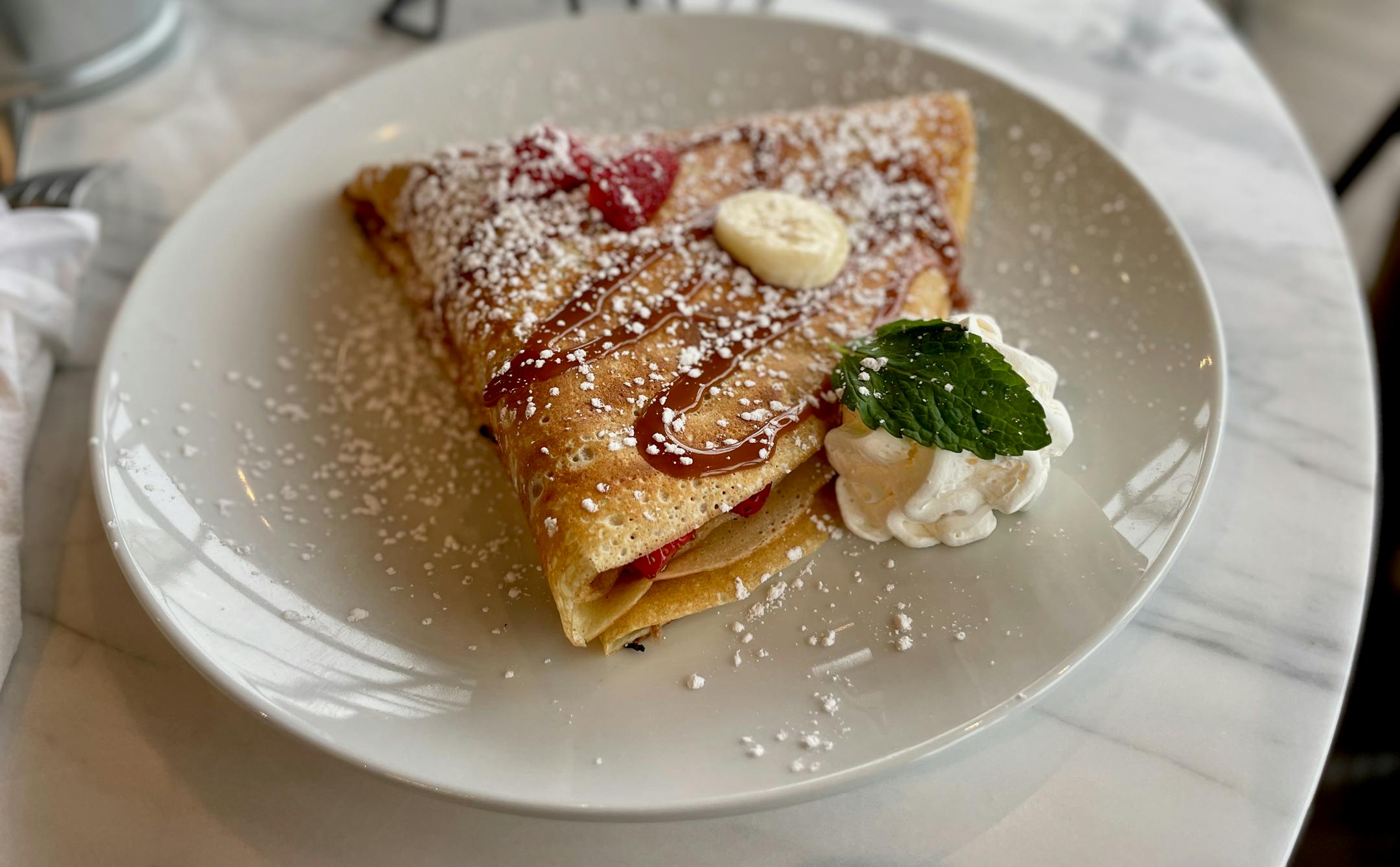 A folded crepe with powdered sugar, a strawberry, whipped cream and caramel.