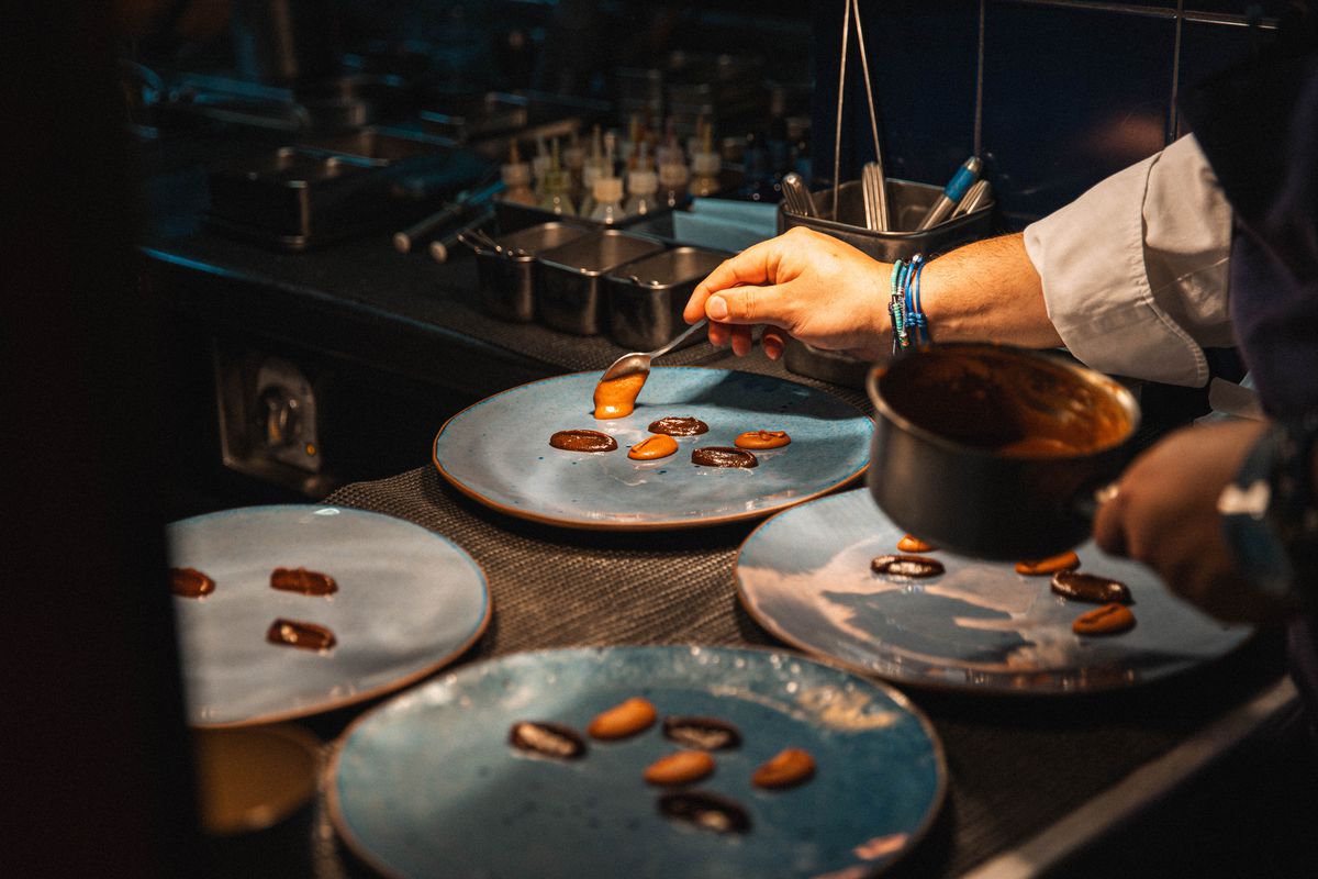 A chef spoons sauces in various shades of brown onto ceramic blue plates.