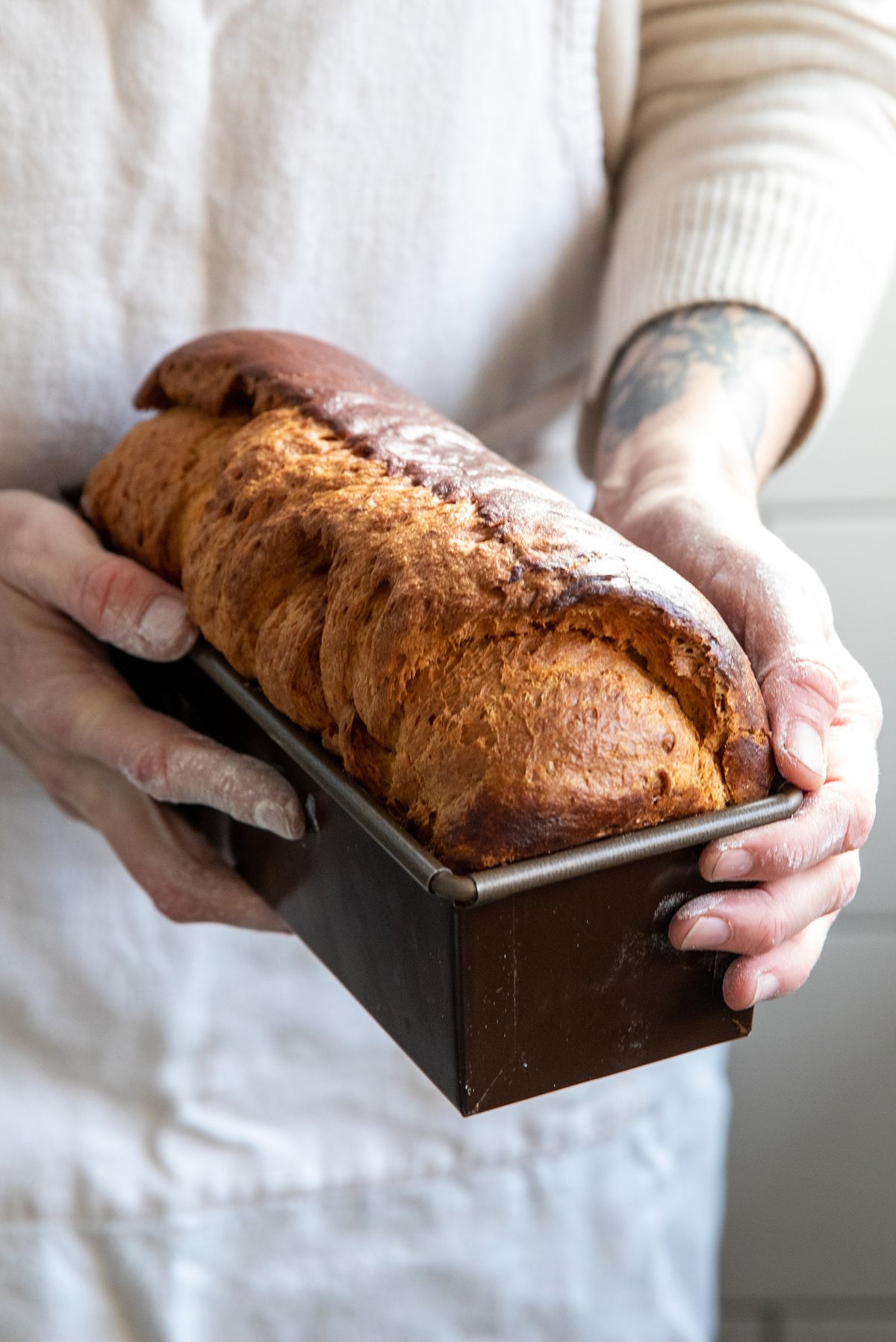 A person holds a loaf of bread in a pan.