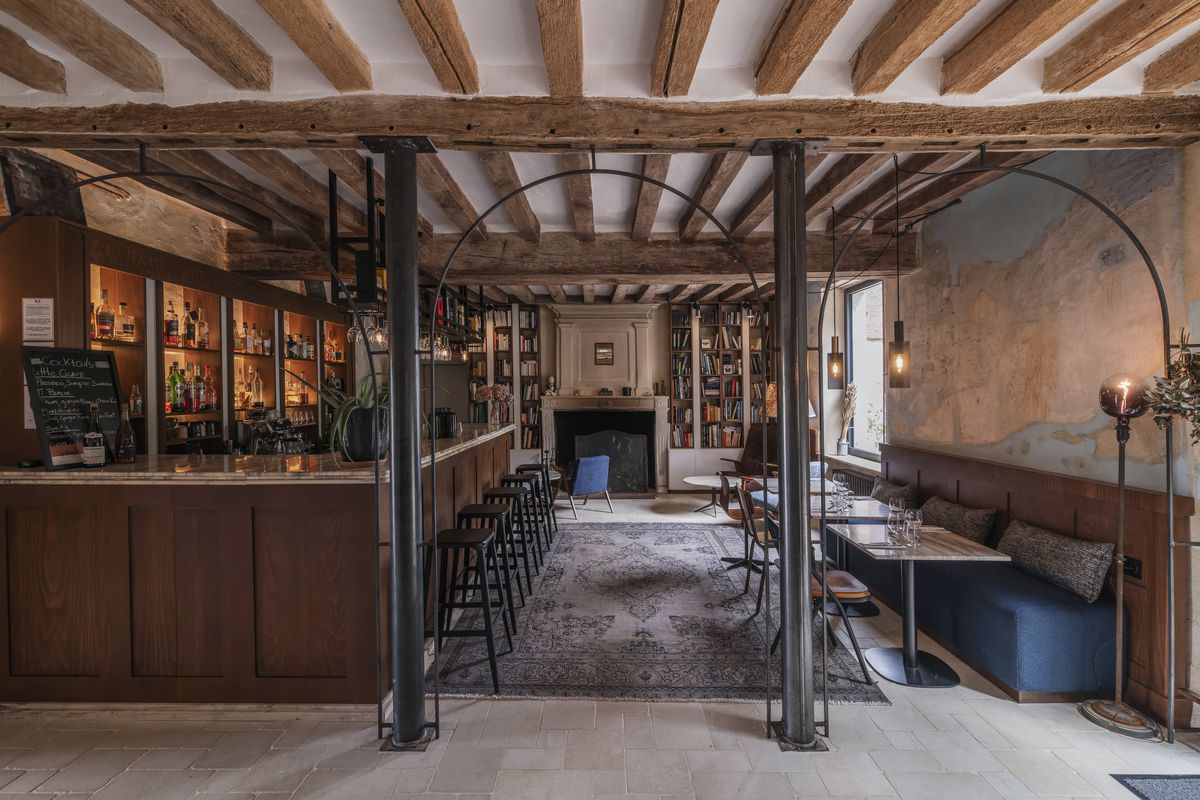 The view through several large wire frame arches into a dining room with a blue leather banquette on one side and a bar on the other, with a library visible beyond. 
