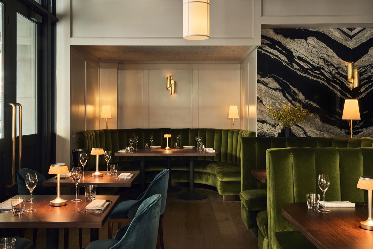 Dark green booths and plush blue seating surrounds dark wood tables in an upscale dining room.