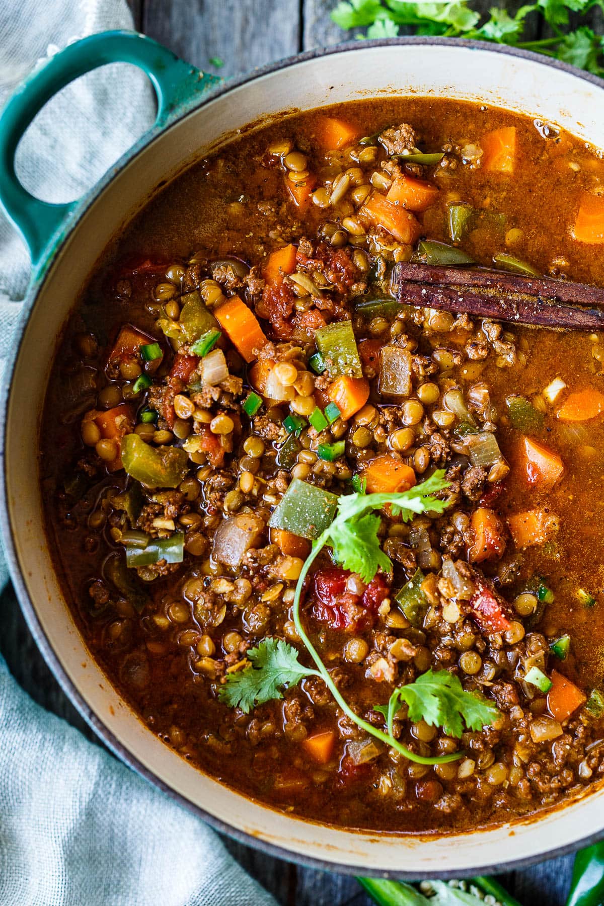 lentil chili vegetable soup in dutch oven, with cinnamon stick and fresh herbs.