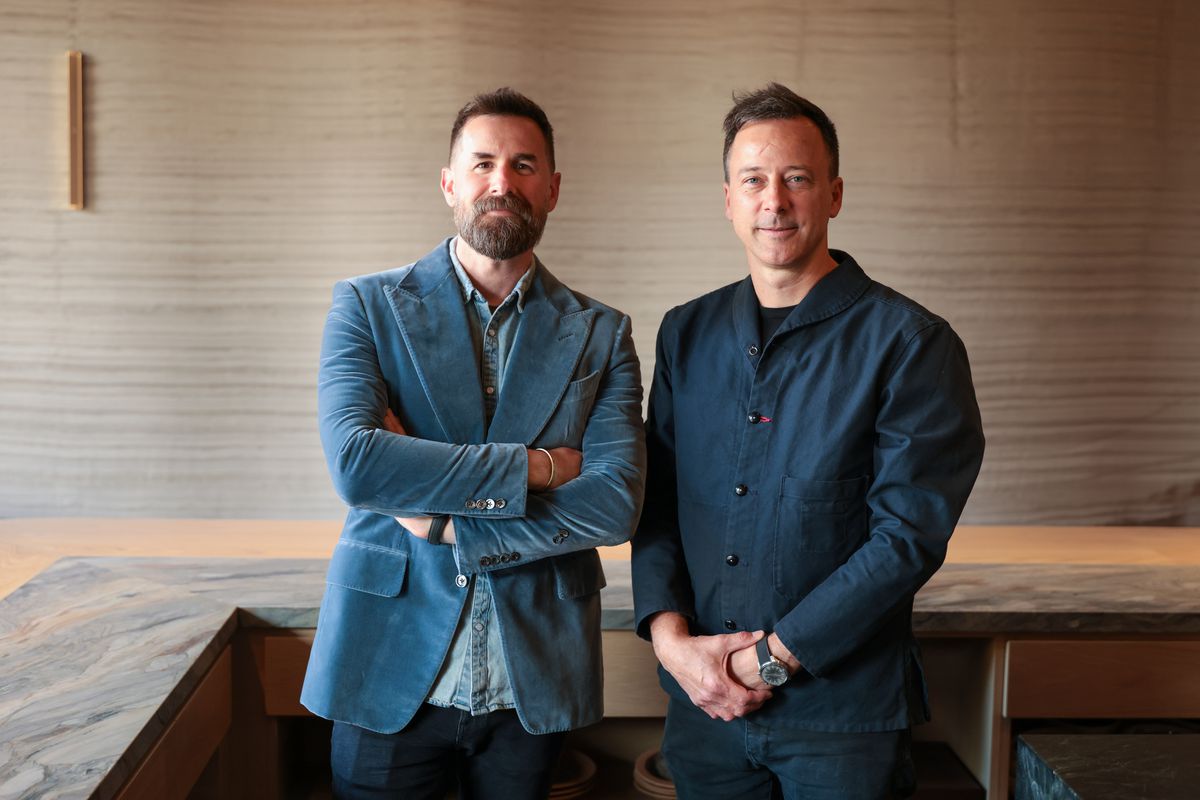 Two men restaurant owners and chef stand wearing blue tops.