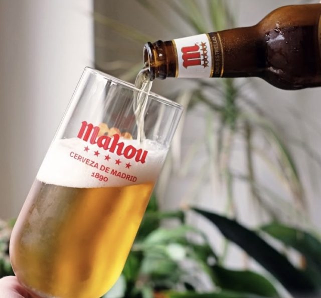 A bottle of Mahou beer being poured into a branded glass