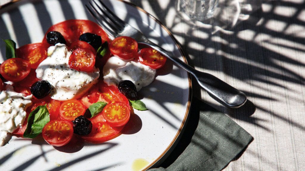 A plate of fresh tomatoes, basil, olives, and mozzarella drizzled in olive oil, the staples of the Mediterranean diet