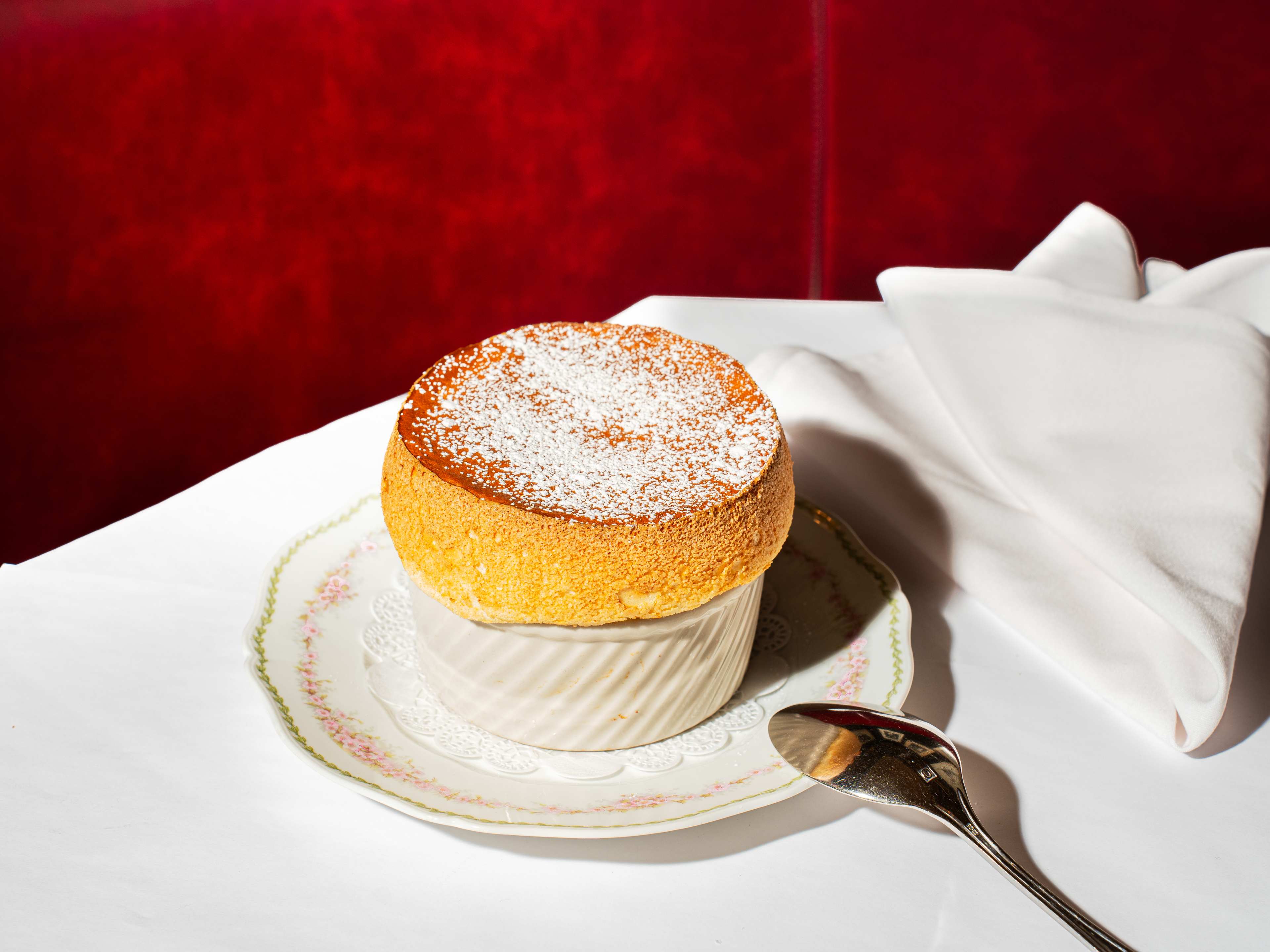 souffle puffed over the edge of a ramekin on a plate with a doily
