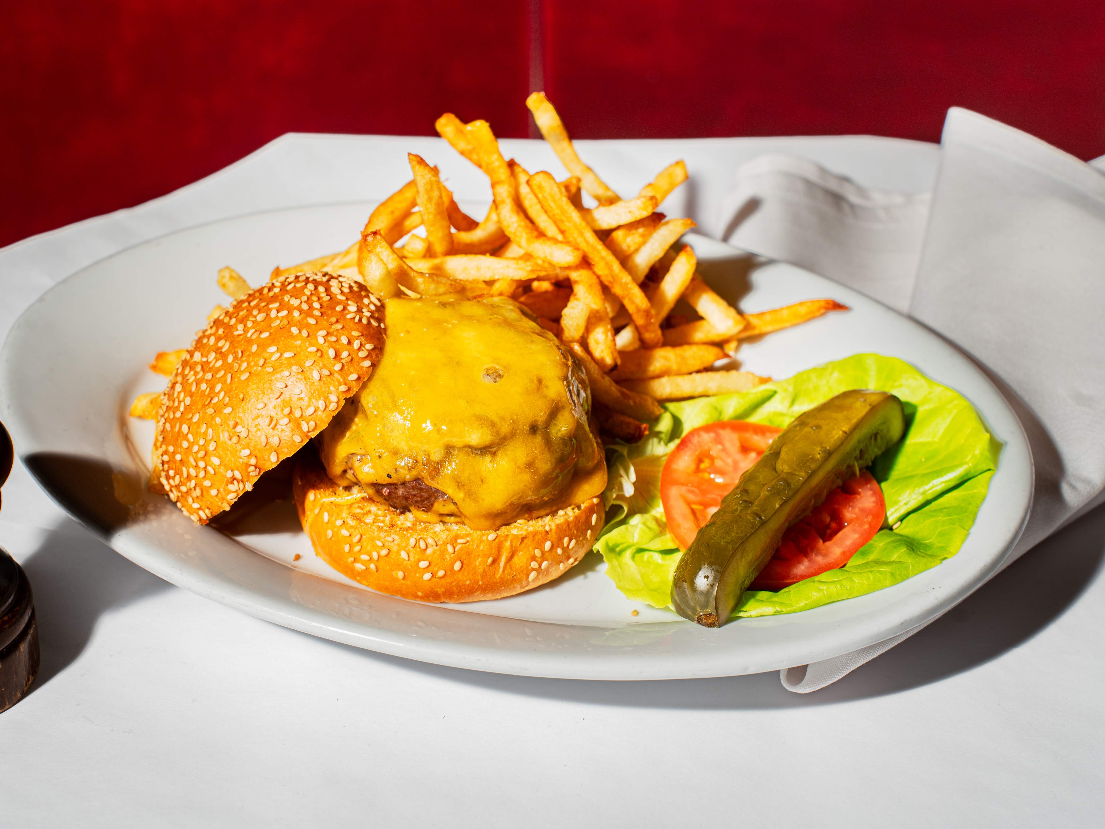burger topped with cheese, with a pickle, tomato and lettuce on the side, and french fries on the plate next to it.