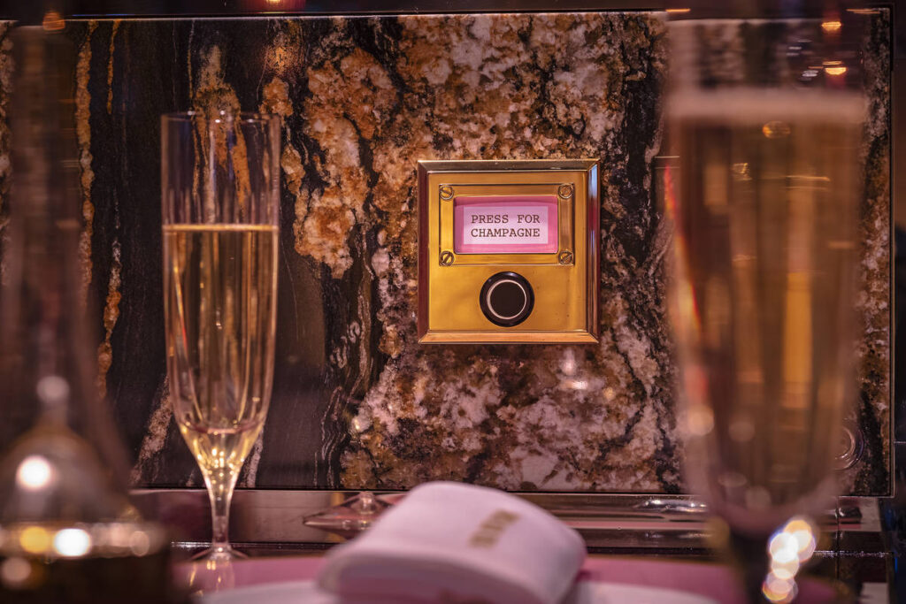 a 'press for champagne button' mounted on the wall of a table in between two glasses of champagne