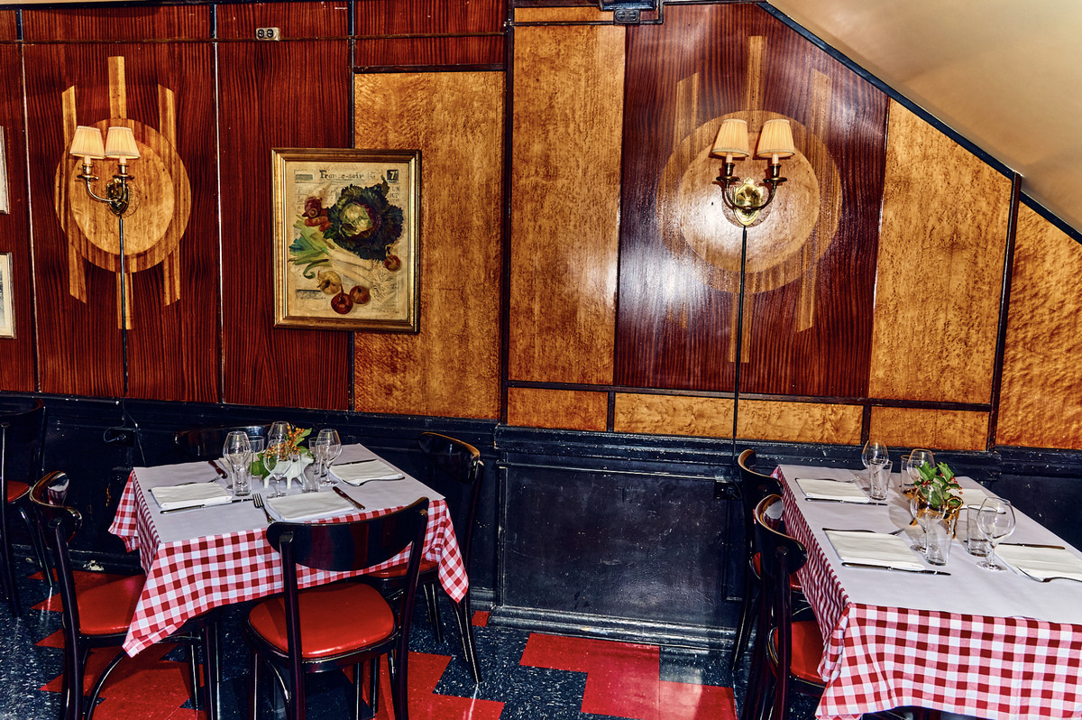 Inside the dining room, with black and red chairs, and tables covers with red and white checked tablecloths. The walls are wood-paneled. And the floors are black and red checked.
