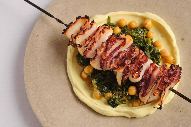 a skewered octopus dish atop chiclpeas, greens, and a puree of sorts