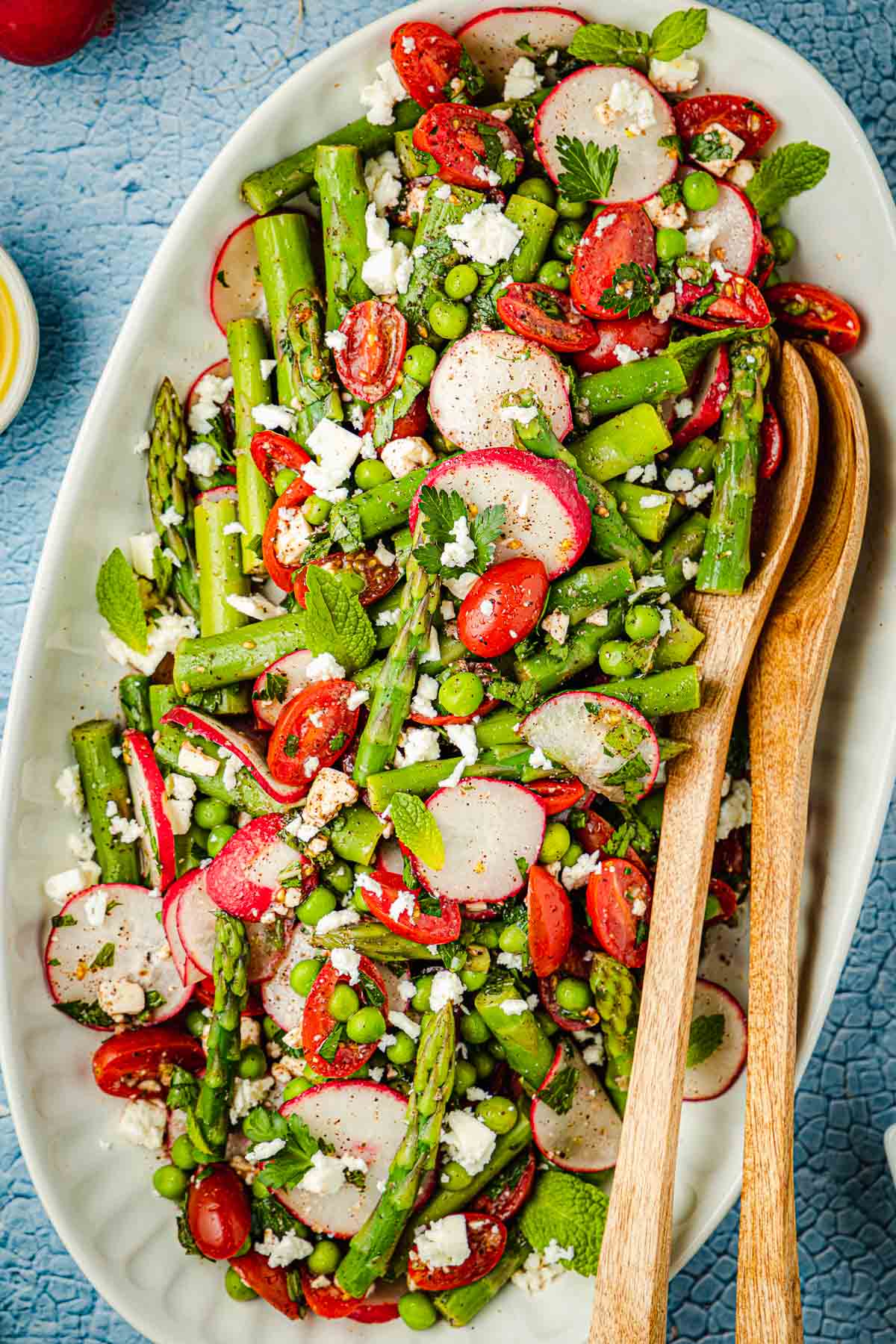 Overhead shot of asparagus salad on a large white serving platter with two wooden serving spoons.