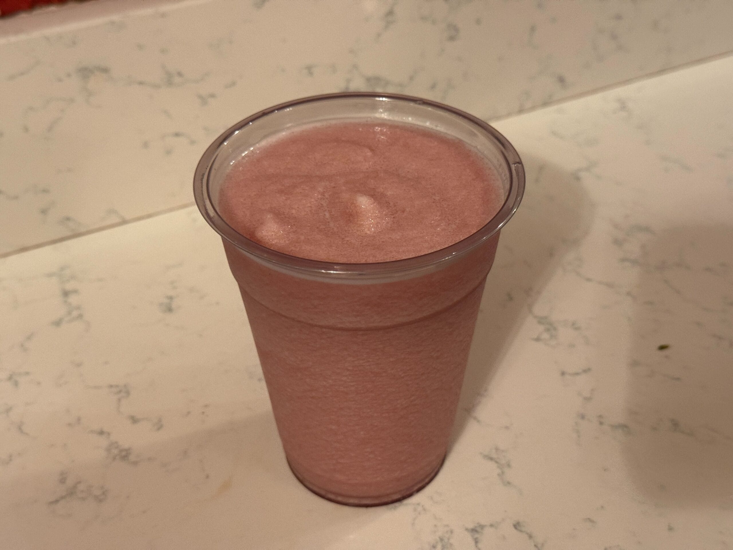 A plastic cup filled with a pink smoothie rests enticingly on the speckled countertop, reminiscent of the delightful treats found at Casey's Corner.