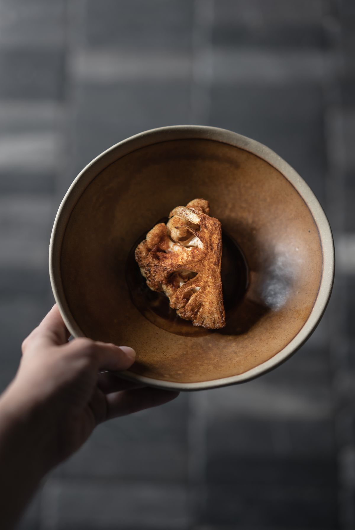 A quarter of cauliflower dusted with spice in a brown bowl.