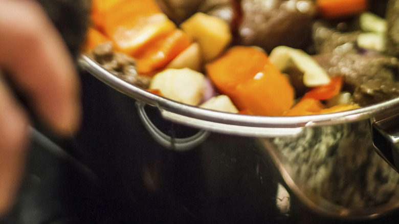 Red wine being poured into a pot full of ingredients.