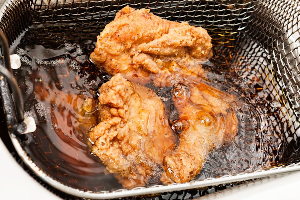 Two pieces of fried chicken cooking in a deep fryer, sizzling in hot oil