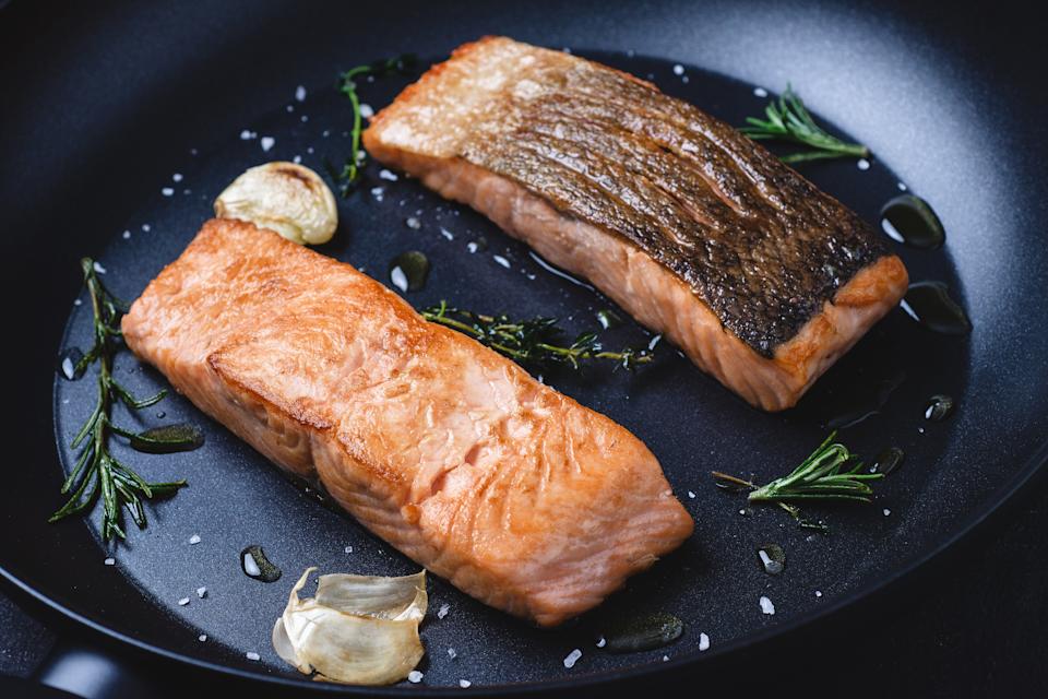 Two salmon fillets, pan-seared with garlic and herbs, are sizzling in a skillet