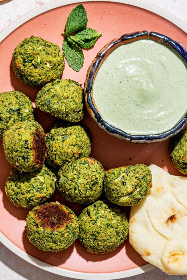 green baked falafel with mint tahini sauce and pita on a pink plate