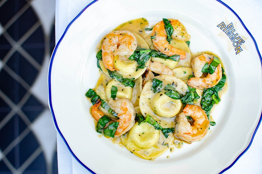 A plate of plump ravioli is tossed with shrimp and strips of spinach in a yellow-brown sauce.