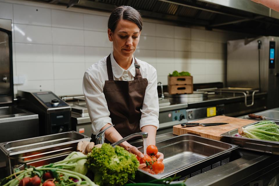 Chef washing vegetables in a commercial kitchen, surrounded by fresh produce and cooking equipment