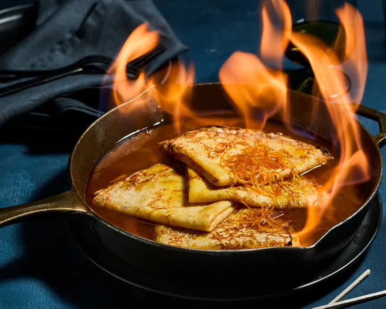 crêpes Suzette in a cast iron pan with candied orange peel and sauce with flames