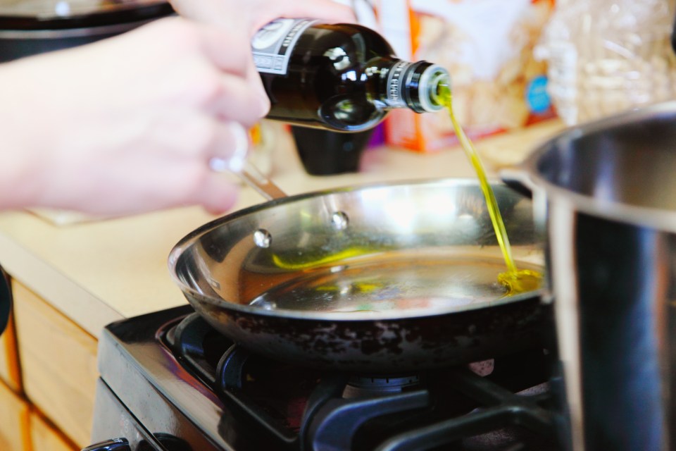 Hand pouring olive oil into a pan on a stove.