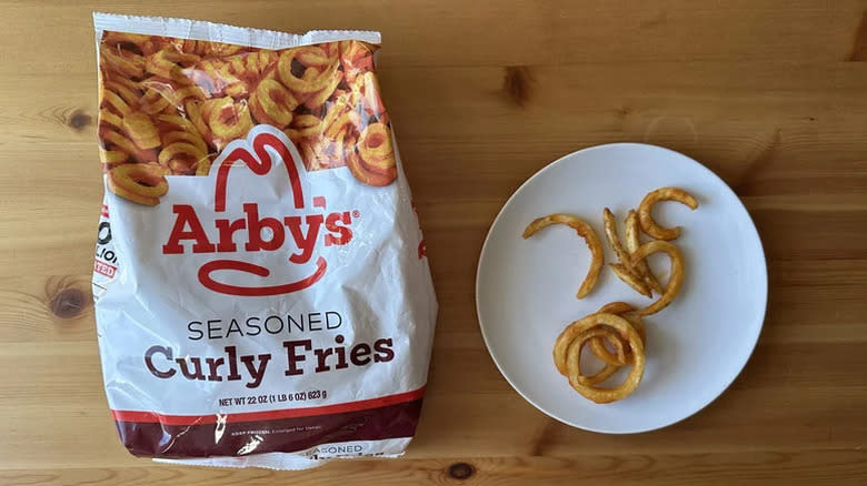 A bag of Arby's Seasoned Curly Fries beside a plant with some fries