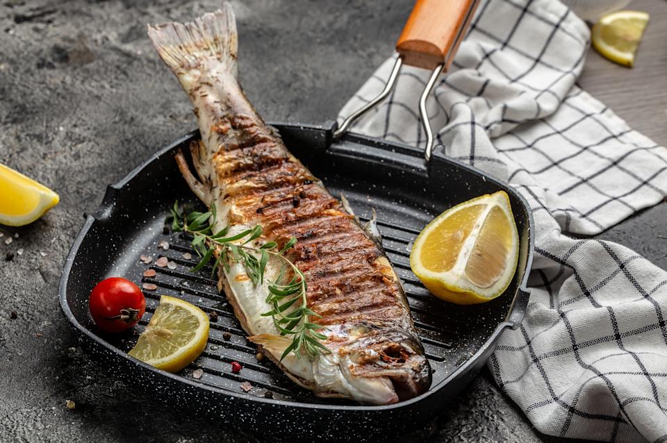 Grilled whole fish on a skillet with lemon wedges, tomato, and rosemary garnish, set on a checkered cloth