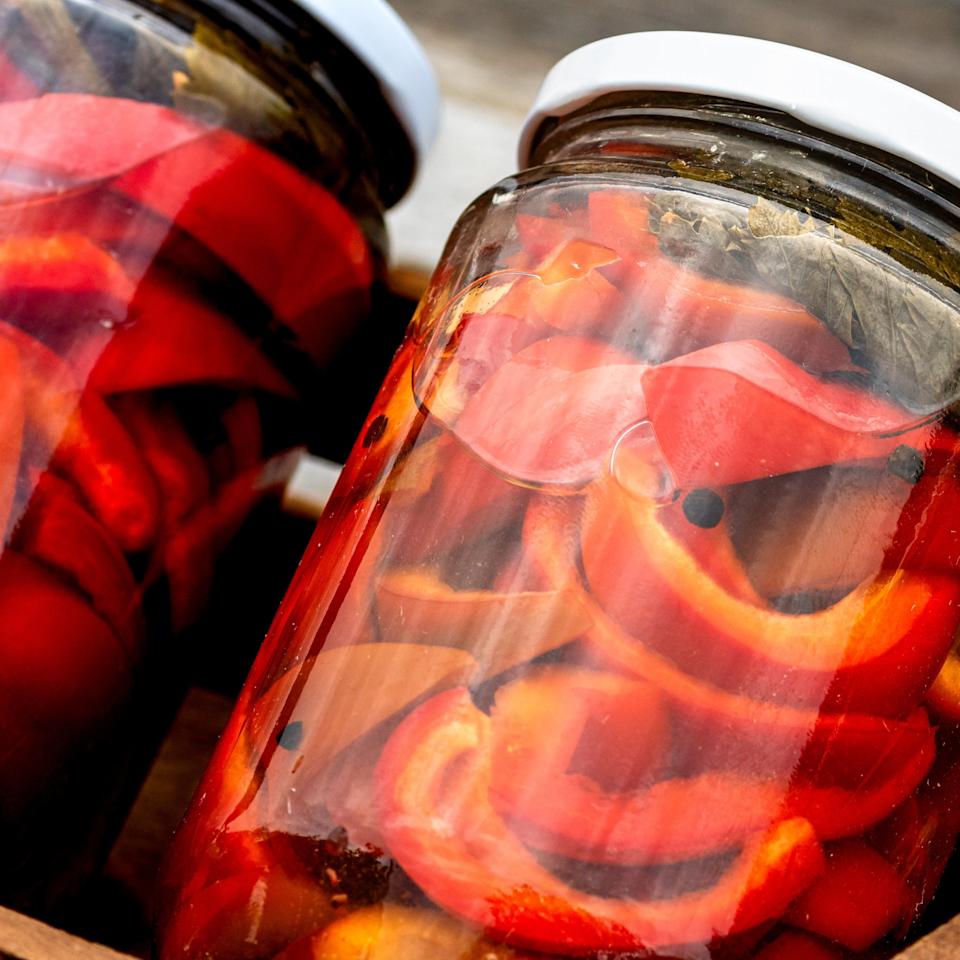 Jars of pickled red peppers in a wooden crate on a wooden surface