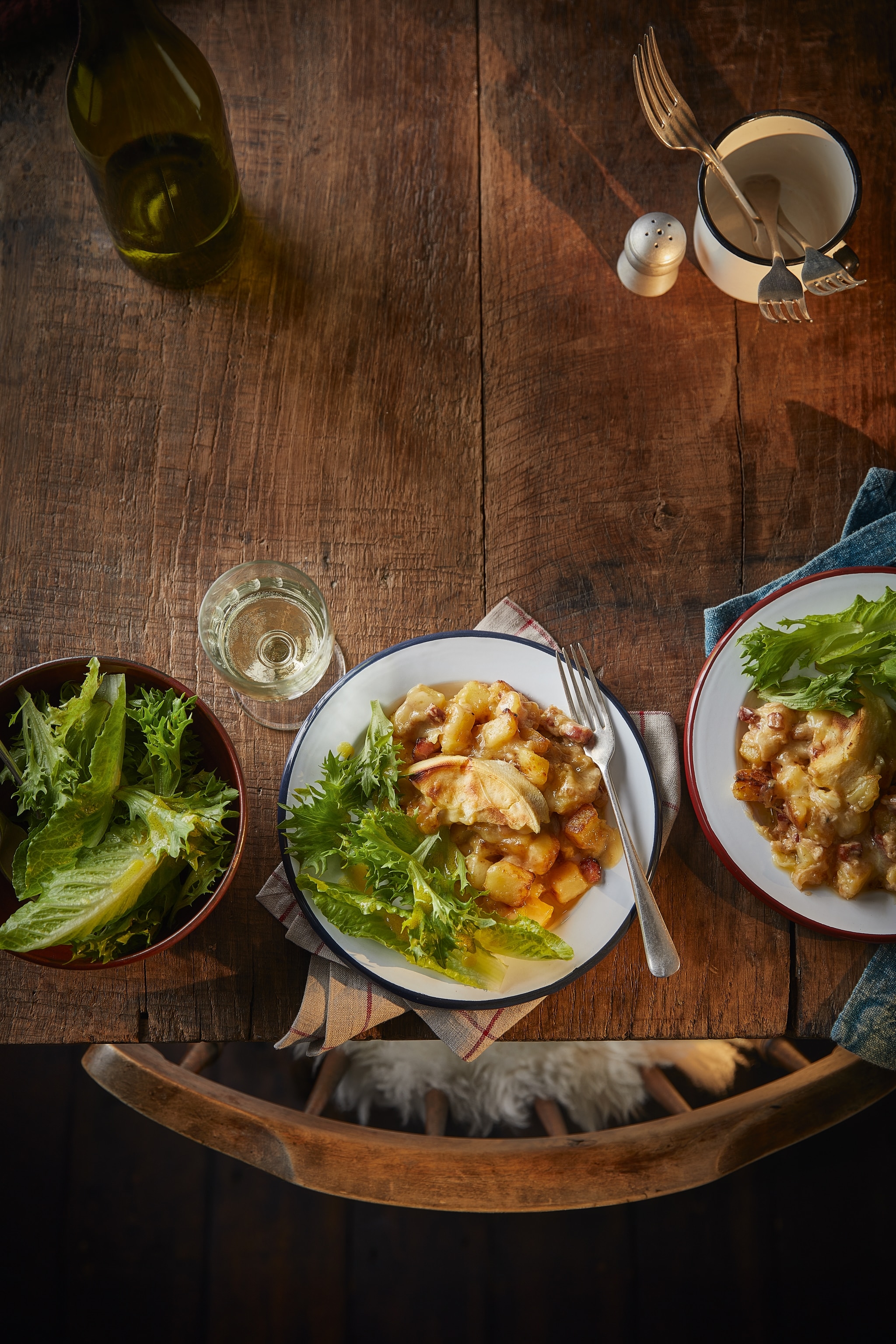 A portion of tartiflette with creamy potatoes, cheese and bacon on a plate with a side of leaves.