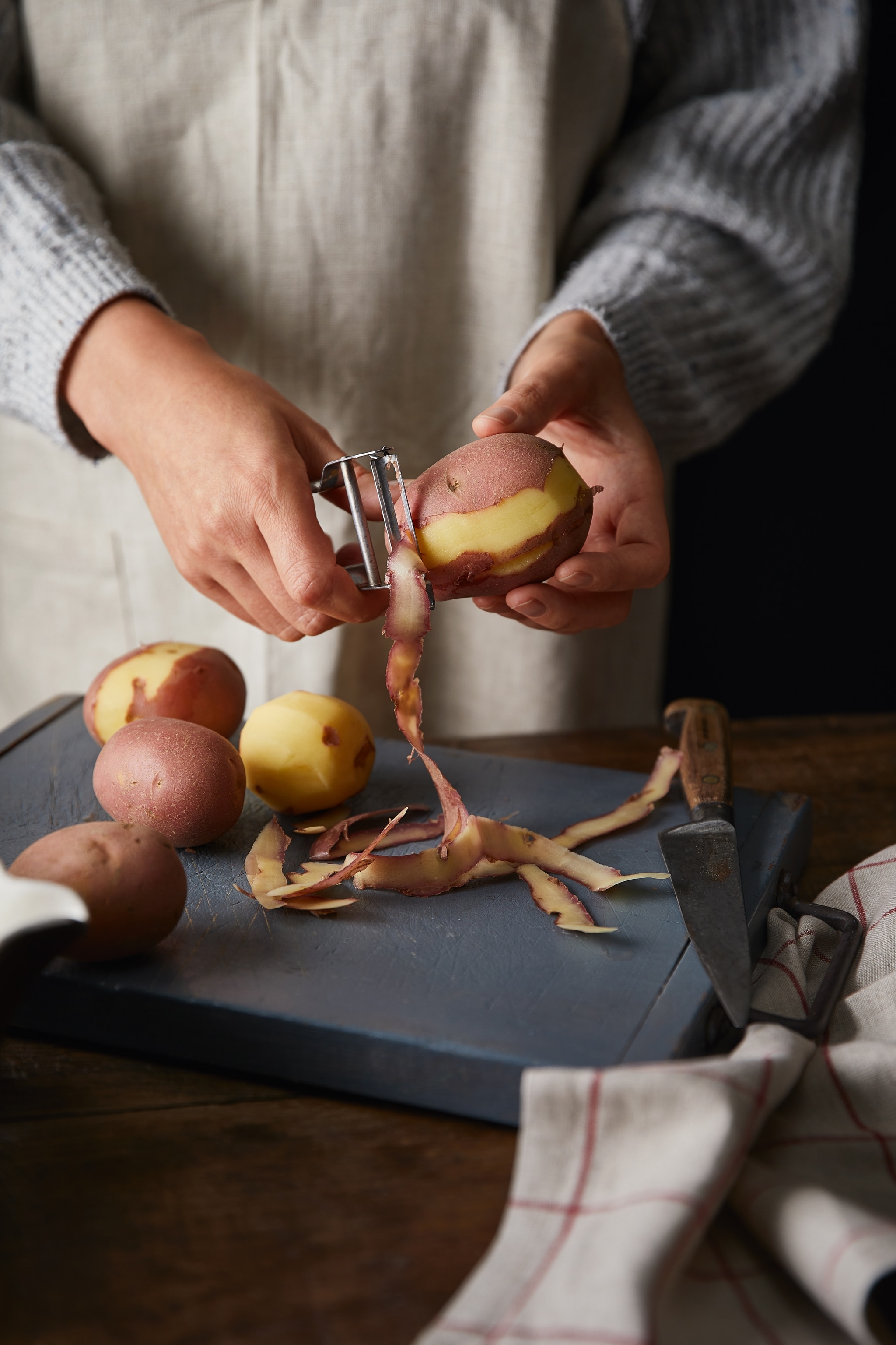 Two hands peeling potatoes on a chopping board.