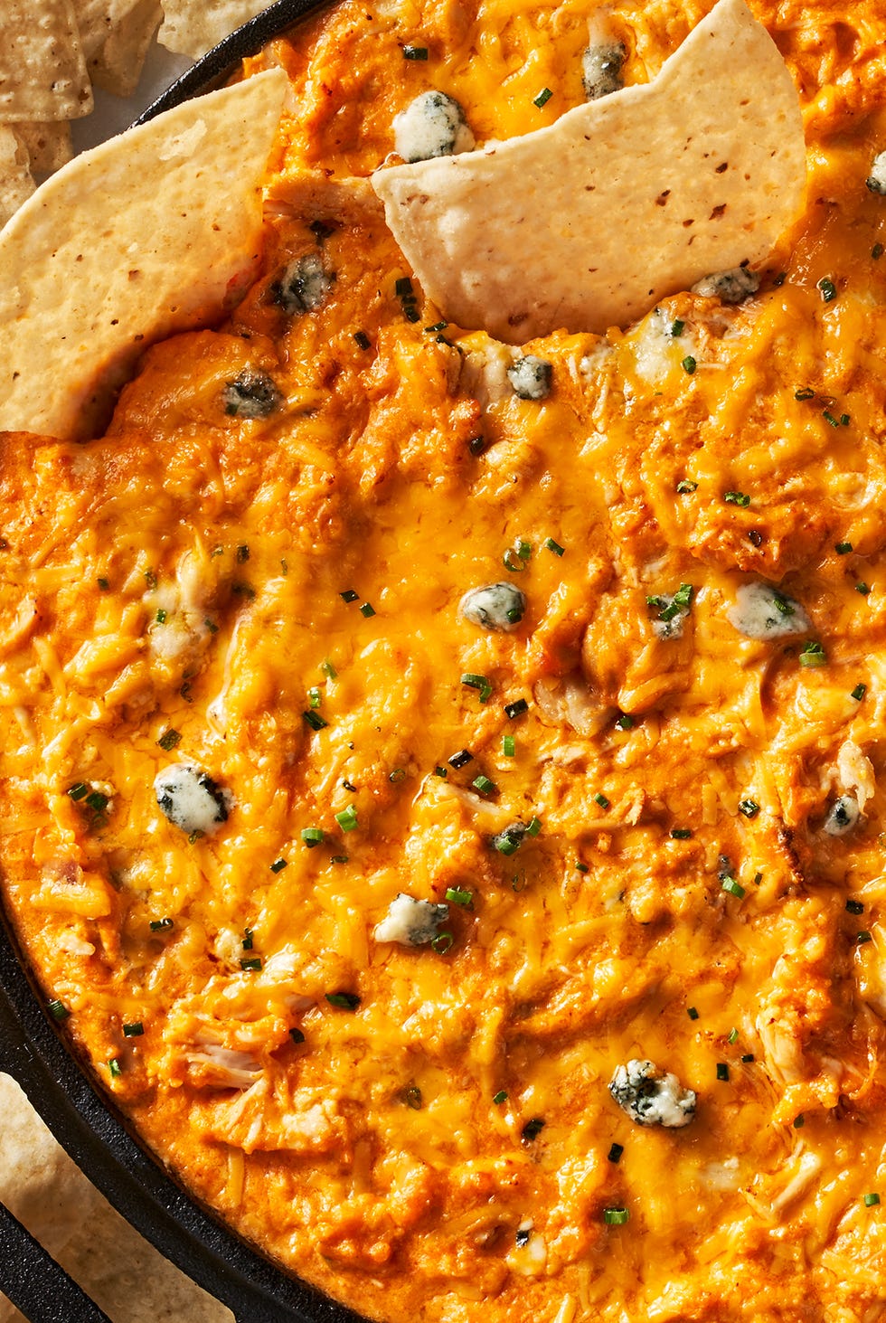 buffalo chicken dip in a skillet beside carrots, celery, and tortilla chips
