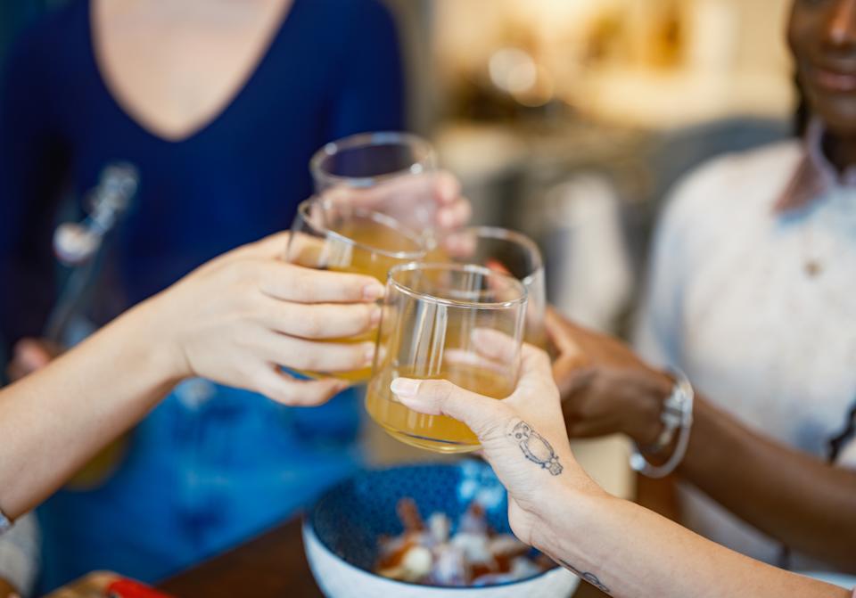 People clinking glasses of light-colored drink over a table with a bowl of snacks