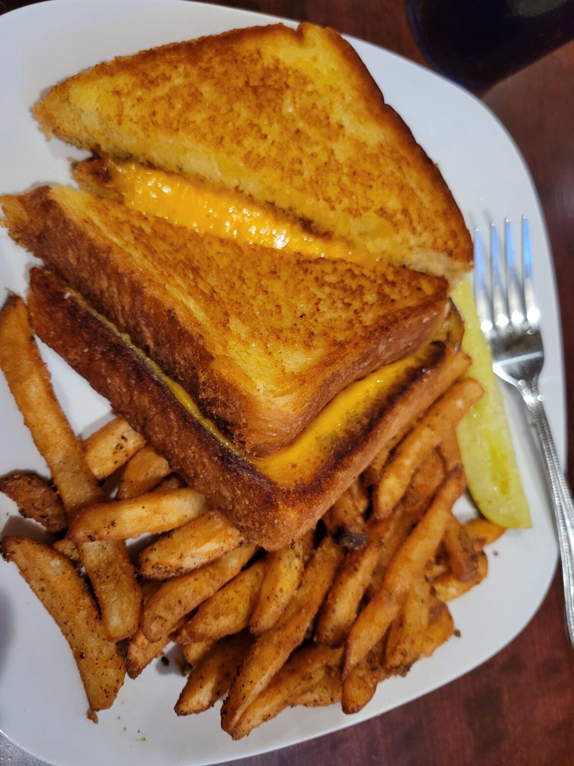 Grilled cheese with seasoned fries, a pickle, and a breadstick.