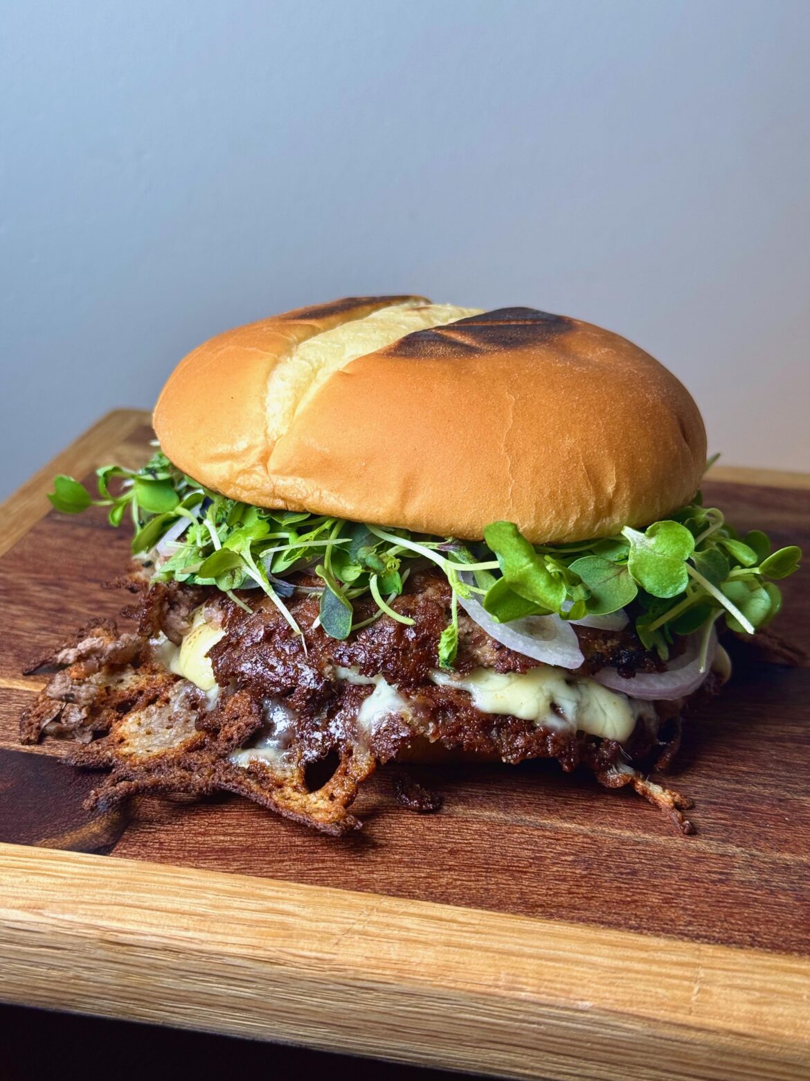 Prime tri-tip ground double smash with shallots, queso chihuahua, and green chile burger sauce and micro greens.