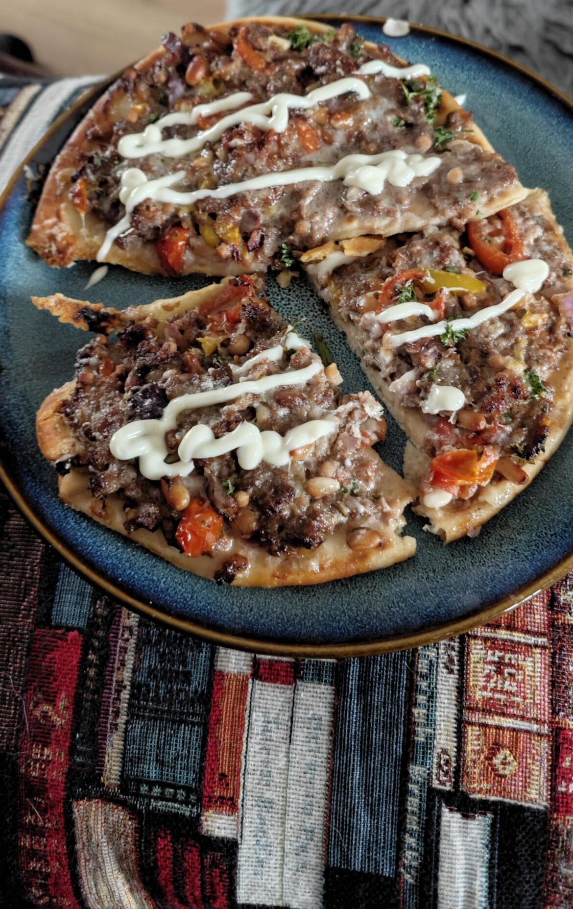lahmajun, flat bread with lamb mince, pine nuts, vegetables, baharat seasoning, toum sauce, and melted cheese