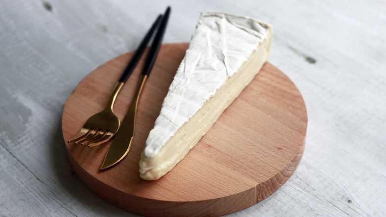 A slice of brie on wooden board with cutlery