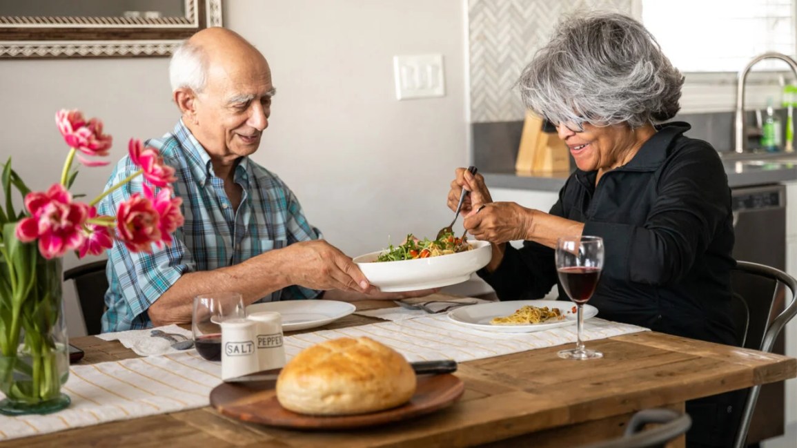 An older couple shares a salad in their dining room