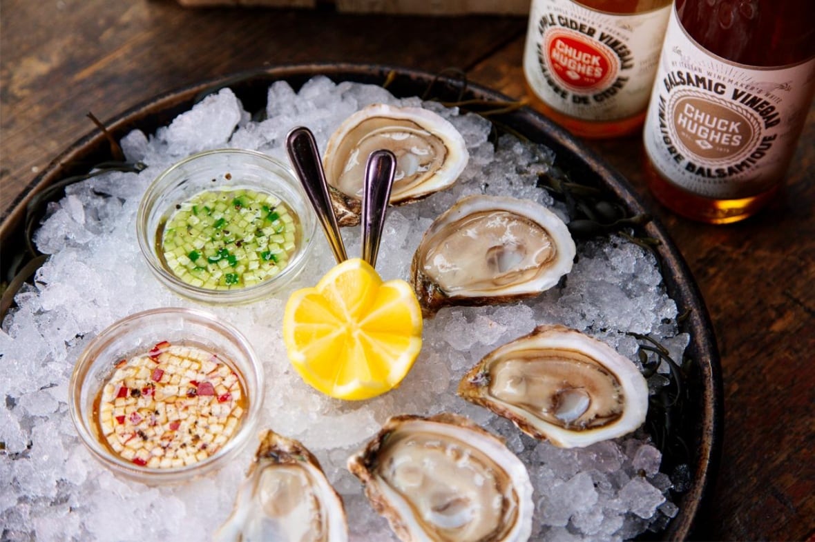Oysters on a platter of ice next to 2 small bowls of Mignonette for dipping. 