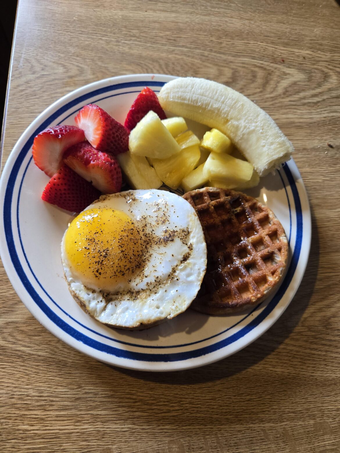 A duck egg on blueberry waffles and some fruit.