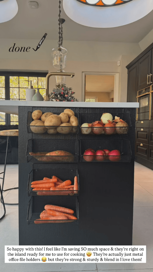 Kitchen island with metal baskets holding potatoes, onions, apples, and carrots.