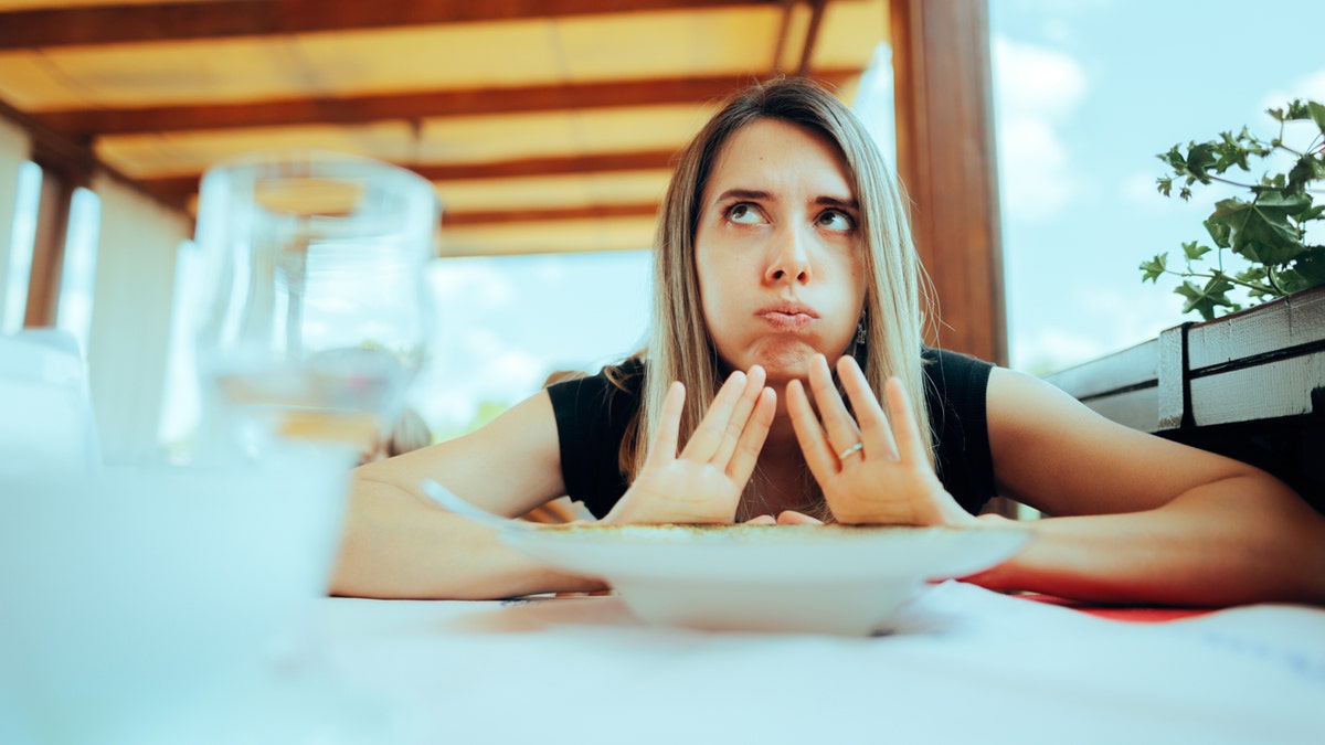 A woman pushes a plate away while having a meal at an outdoor restaurant.