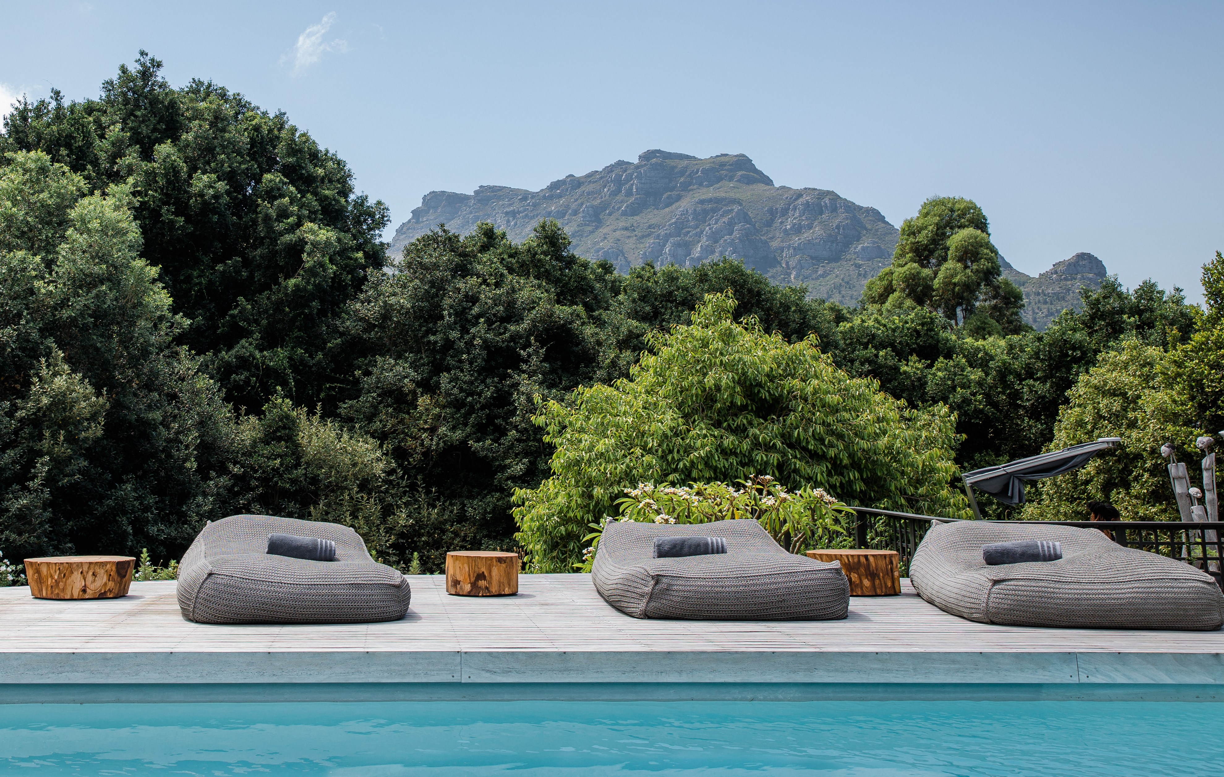 Four lounge chairs by a pool overlooking a mountain and trees.