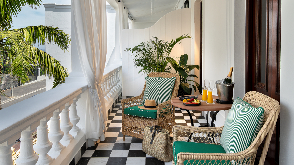 Hotel balcony with wicker chairs, a table, and champagne.