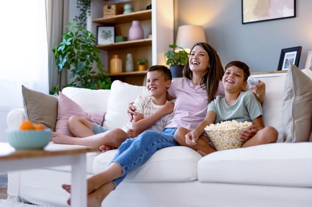 A mother and her two sons sit on the sofa enjoying a home movie night