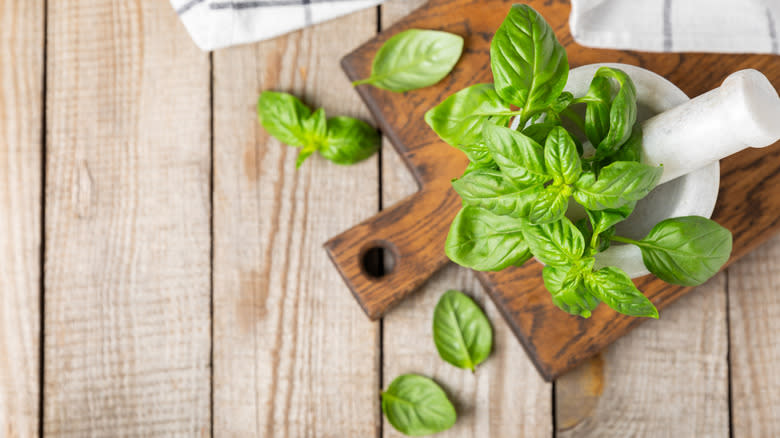 Basil in a mortar and pestle on a wooden background.