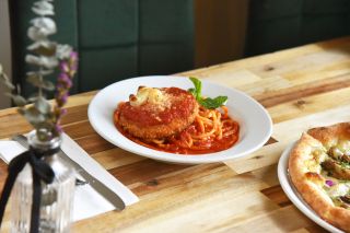 vegan chicken parmesan sits next to a pizza on a wood table